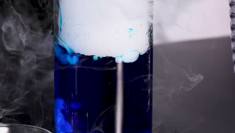 a vibrant blue liquid reacts, creating bubbling and swirling smoke effects in a glass container.