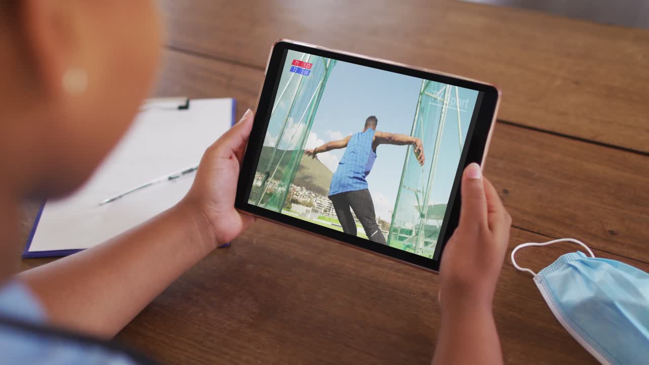 태블릿에서 육상 디스크 이벤트를 시청하는 얼굴 마스크와 함께 테이블에 앉아있는 여성의 합성