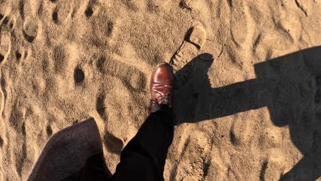 brown leather shoe stepping on soft golden sand in sunny daylight