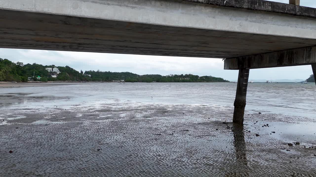 A drone captures a tranquil scene of a pier in Phuket, Thailand, with overcast skies and calm waters, highlighting the natural beauty