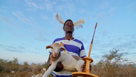 close-up portrait of karamojong warrior carrying baby goat in uganda, africa.