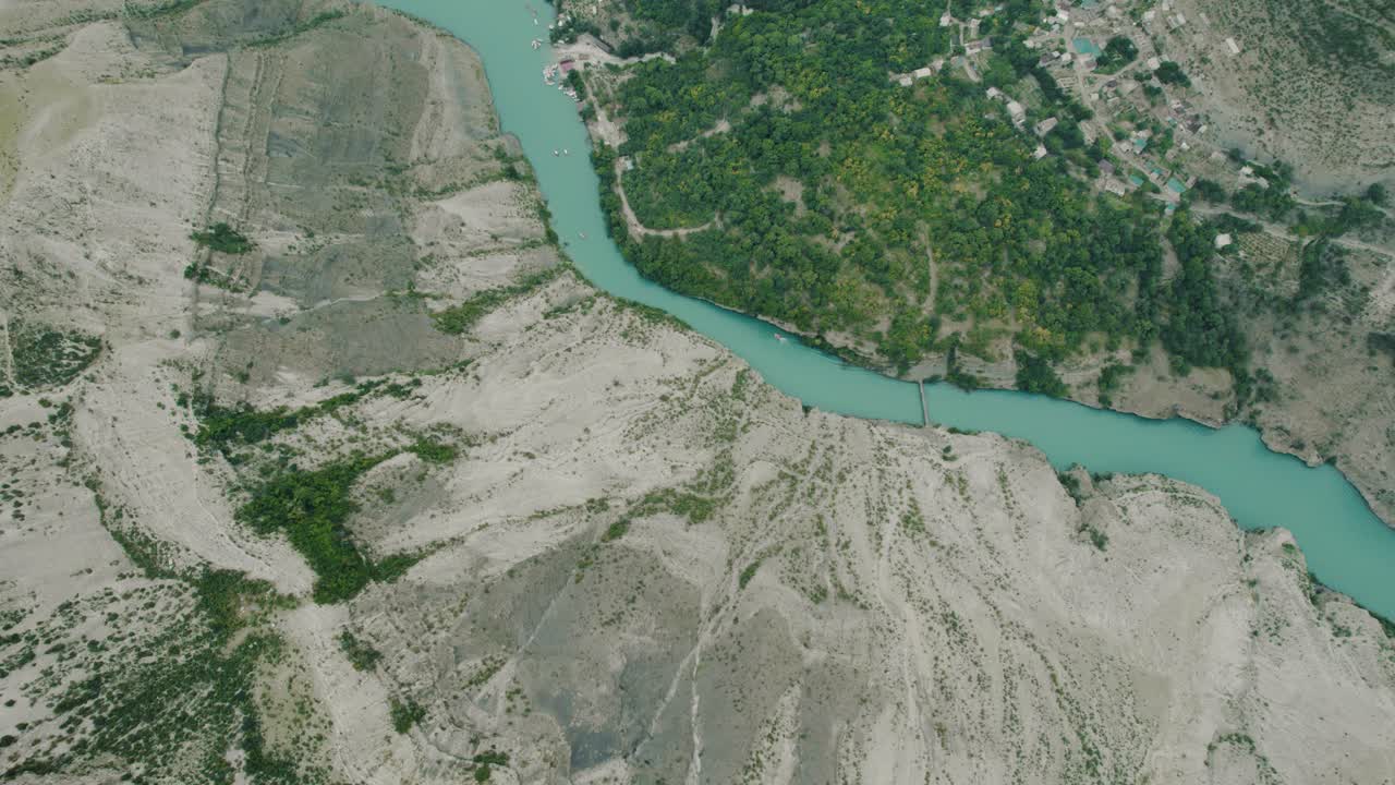 воздушный вид на бирюзовую реку, извилистую через каньон с деревней, расположенной в долине.