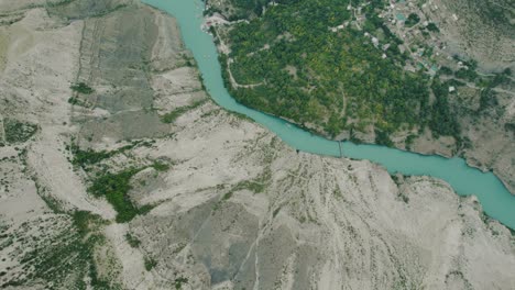 aerial view of a turquoise river winding through a canyon with a village nestled in the valley.