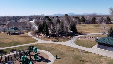 Drone-Volando-Hacia-Atrás-Lejos-De-Un-Parque-Y-Un-Patio-De-Recreo-Donde-La-Gente-Y-Los-Niños-Están-Jugando