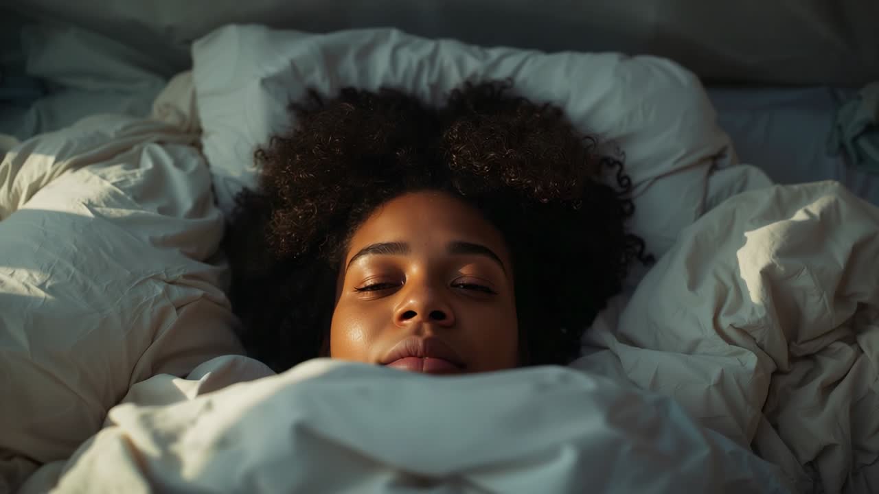 Vågnende kvinde, der åbner øjnene og blinker i sengen, reagerer på morgenlyset under den hvide dyne
