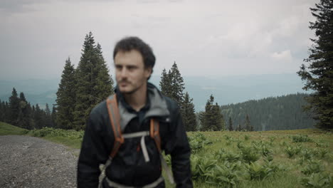 hiker walking on a macadam road with a backpack, wearing a wind and rain proof jacket