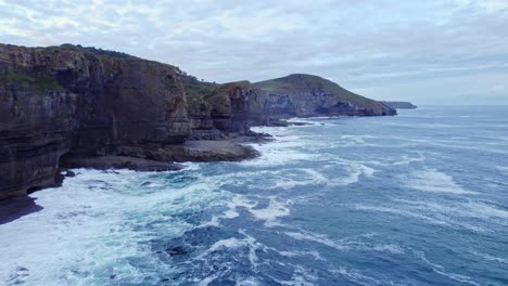 -Drone-capture-the-coastline-of-the-island-of-Isla,-Cantabria-from-the-sea-level-on-a-sunny-day