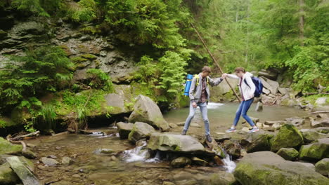 a young couple of tourists with backpacks crosses a mountain river in the forest hd video