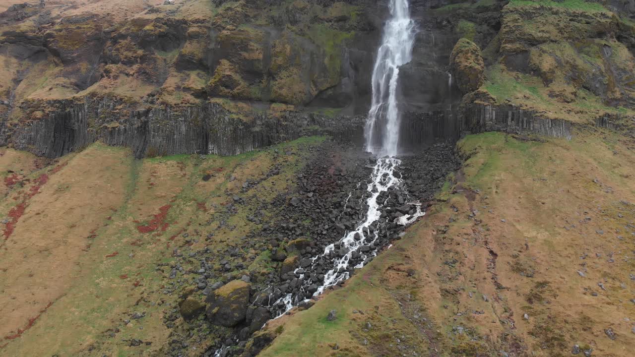 Flying in towards the tall waterfall Bjarnarfoss showing the dark basalt rock columns surrounding this nature wonder in the western part of Iceland