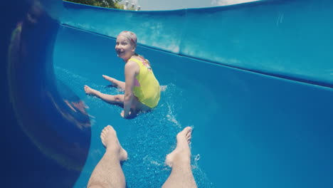 una familia feliz con un niño está montando un tobogán de agua riendo agitando sus manos a la cámara lenta m
