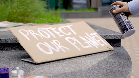 close up of a hand scribbling something on a placard using a spray paint can