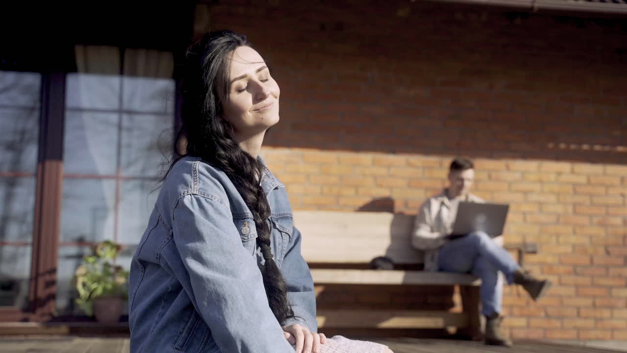 그녀의 파트너가 시골 집 밖에서 노트북을 사용하고 있는 동안 코카시안 여성이 개를  ⁇ 고 있습니다.