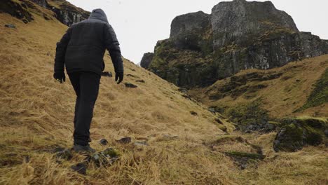 ángulo bajo del hombre caminando sobre la hierba amarilla paisaje islandés hacia el acantilado volcánico