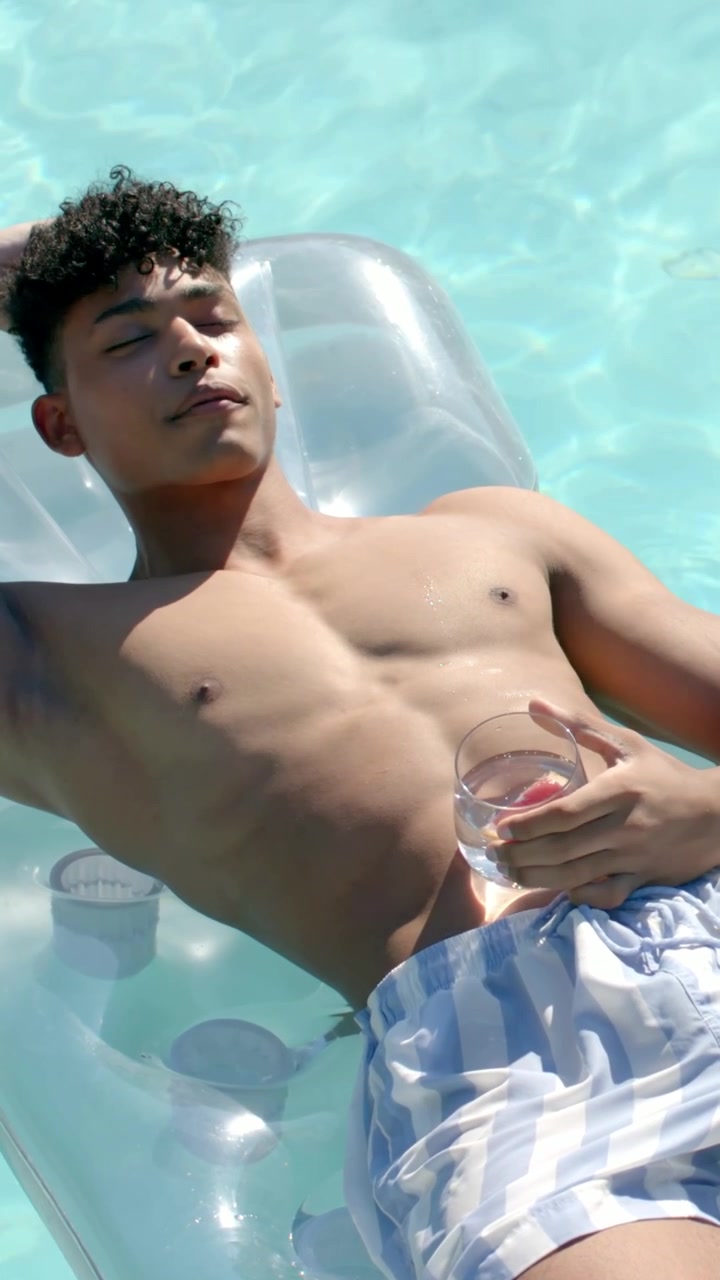 Camera pulling back revealing male reclining on clear float holding glass, relaxing under sun in 3D