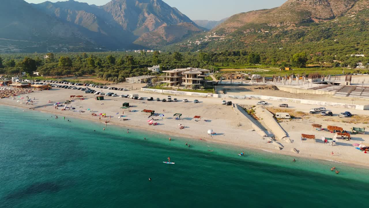 A vibrant beach with paddleboarders and tourists enjoying clear turquoise waters, aerial view
