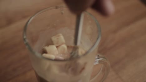 Stirring-glass-mug-of-hot-chocolate-with-marshmallows-and-whisk