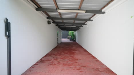 gran acceso lateral a la piscina tropical con césped de spa bajo sombra de metal ondulado y camino de ladrillo