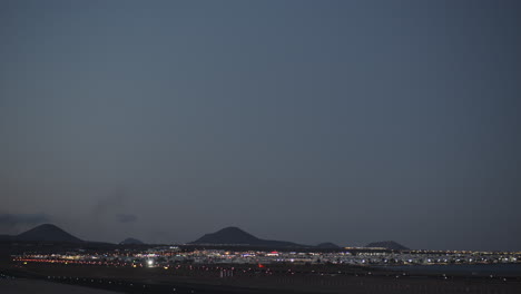 Una-Hermosa-Vista-Nocturna-Con-Un-Avión-Despegando-Sobre-La-Ciudad-Nocturna-Y-Montañas-Oscuras