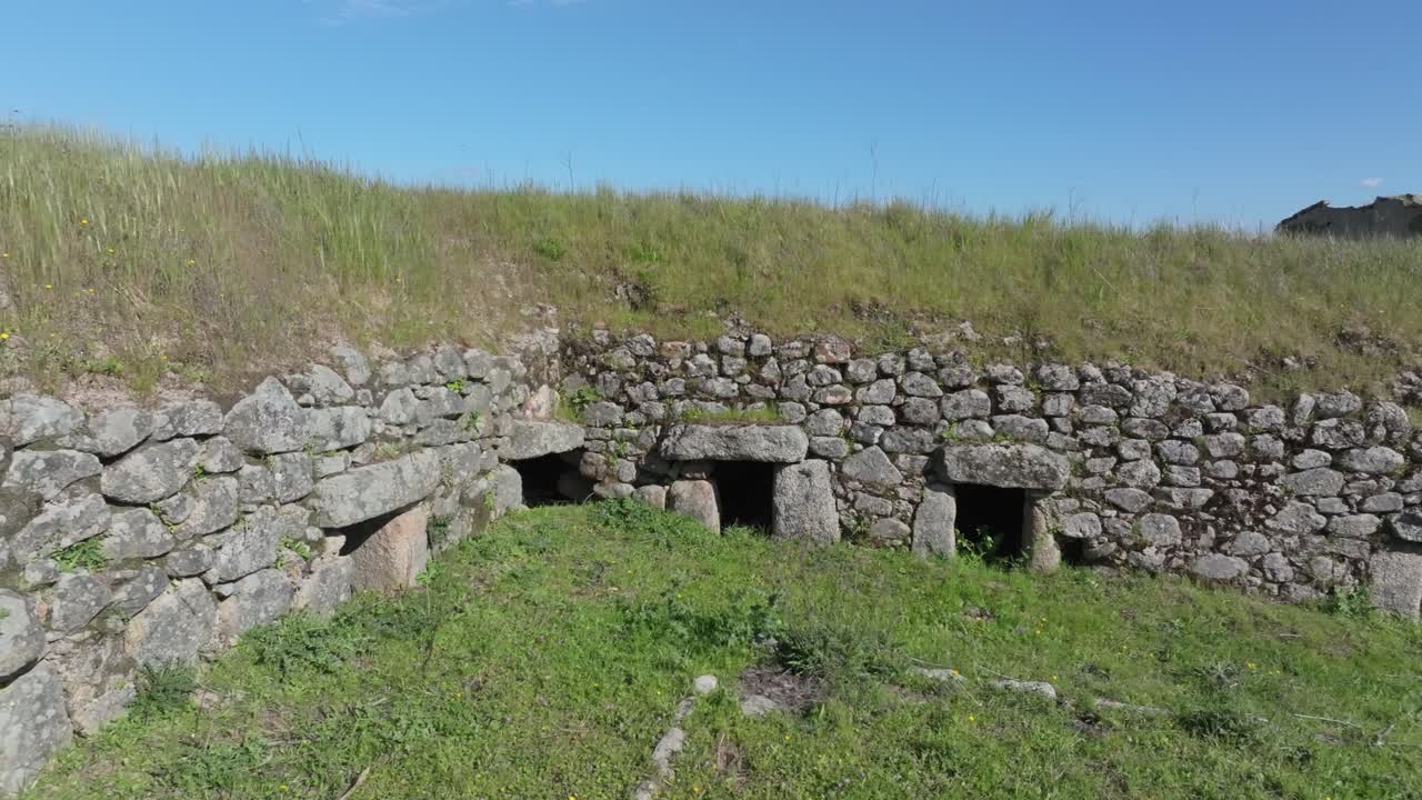 Lateral drone flight inside an 18th-century stone structure used for pig farming. Multiple side entrances with lintels visible. Grass has grown on the roof, showing signs of age and abandonment.