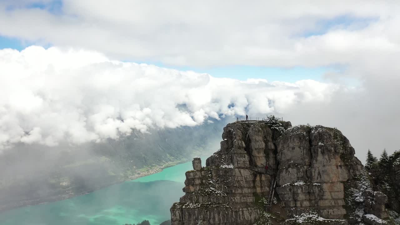 하얀 푹신한 구름, 무성한 산비탈, 쉬니게 플라테(schynige platte)의 거대한 강이 있는 놀라운 풍경이 내려다보이는 산 정상에서 하이킹을 한 후 남자가 혼자 서 있습니다.