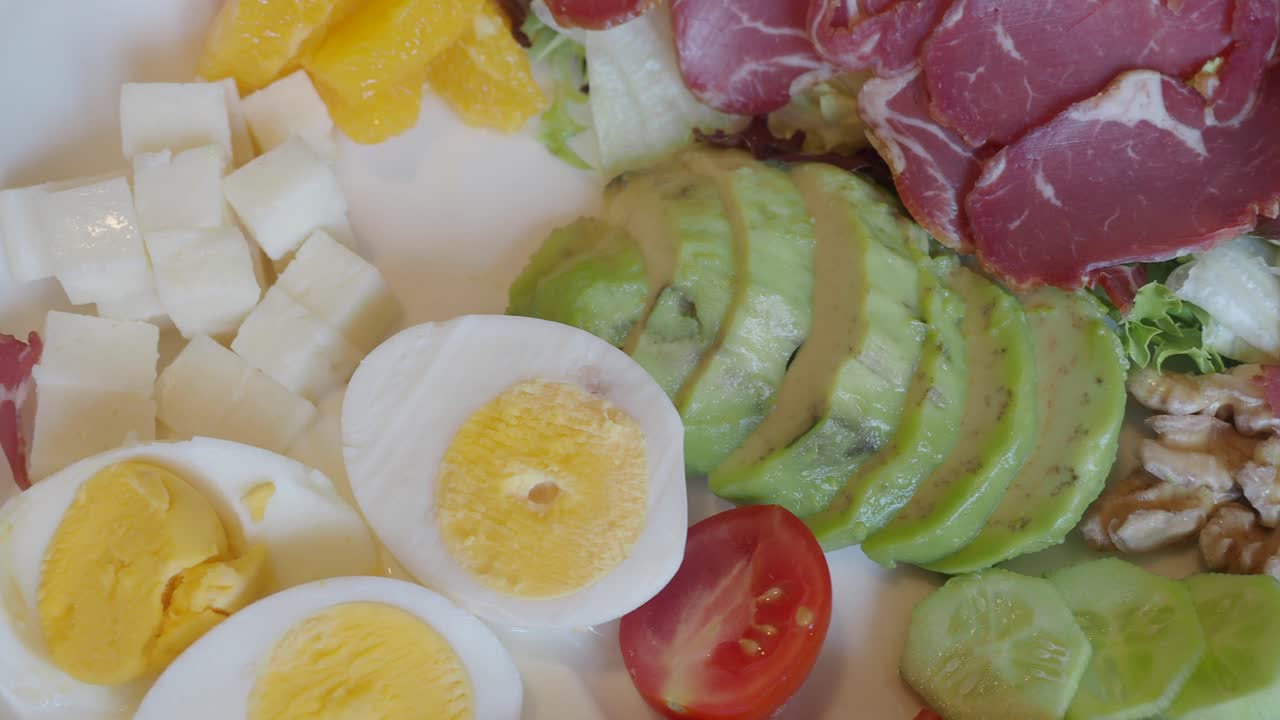 Salad with avocado, egg, ham, orange, tomato and cucumber