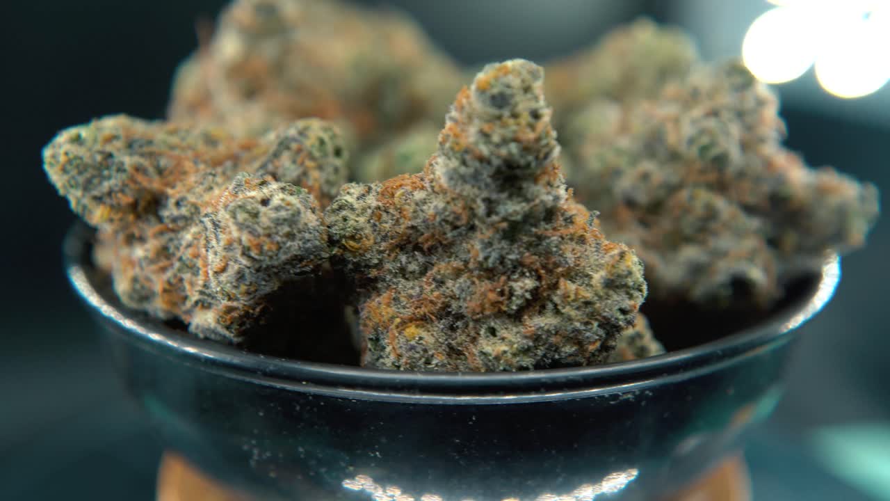 A hyper macro dreamy tilt up shot of a cannabis plant, hybrid orange strains, sativa ,marijuana flower, on a rotating stand, slow motion, 4K video, studio lighting