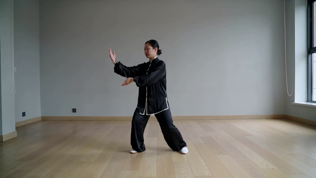 Una praticante donna che entra e pratica Tai Chi in una sala con uniforme nera e scarpe bianche.