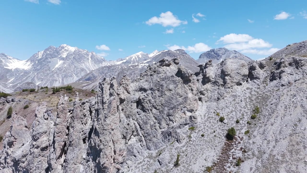 Scharfe graue Felstürme des Jalet-Gipfels ziehen vorbei, mit schneebedeckten Ortler Alpenkämmen im Hintergrund an einem klaren Sommertag.
