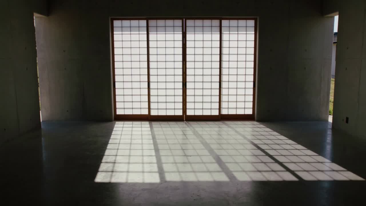 Sollys bevæger sig gennem en 4-panels shoji-dør og kaster et voksende gitter hen over betongulvet i et tomt rum.