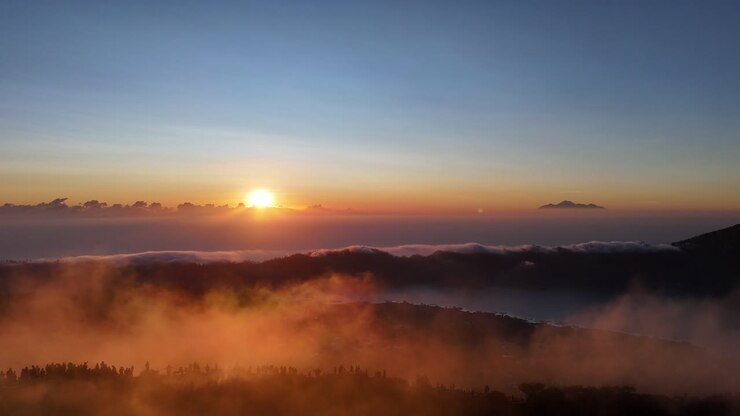 A golden sunrise cast light over Mount Batur in Bali, Indonesia, with hikers gathered at the summit to witness the mist veiling volcanic peak and glowing clouds