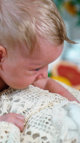 beautiful blond caucasian infant boy in yellow pants. blue-eyed baby struggling to raise head. close up. blurred backdrop. vertical video