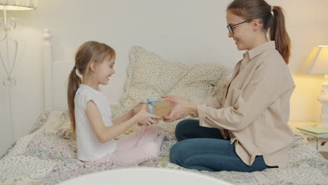 mother and daughter giving and receiving gifts in a bedroom