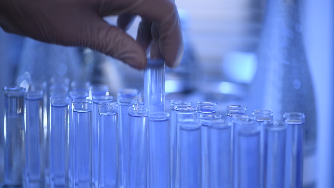 Mano guantata che raccoglie una provetta in un laboratorio