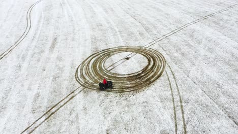 the adult person on an atv in a snow-filled farm field - aerial view