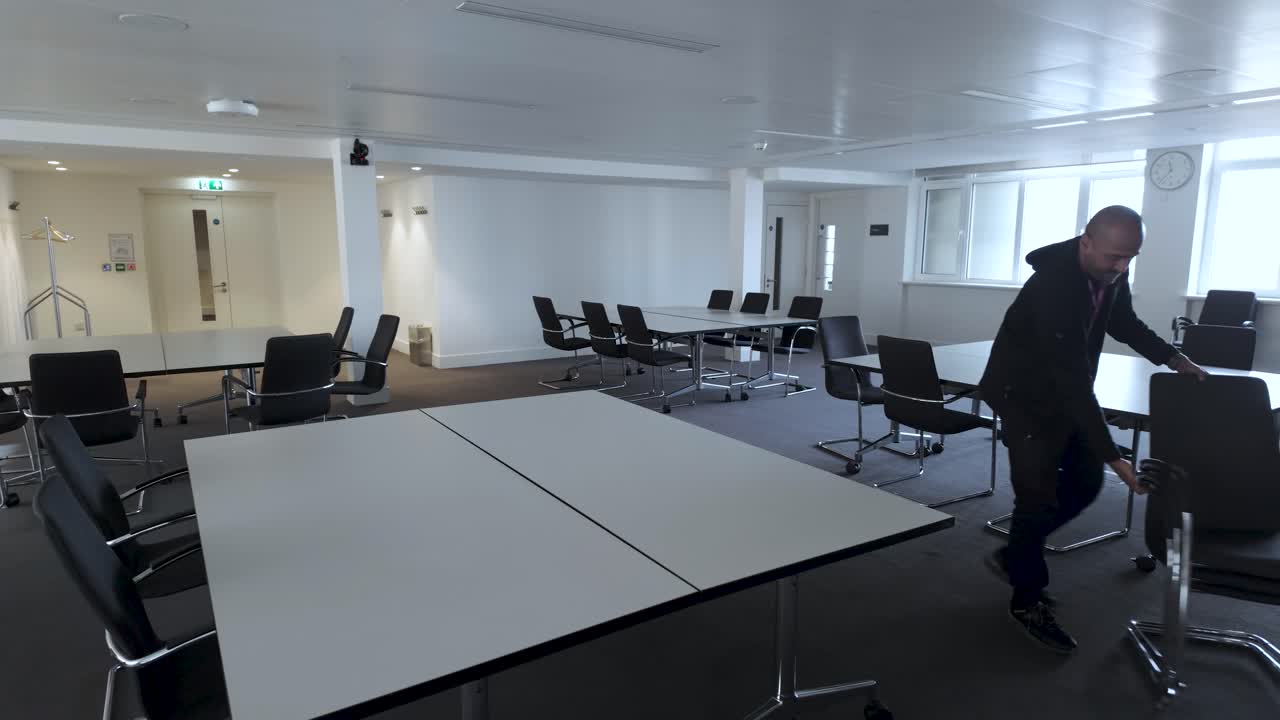 Office Facilities Worker rearranges chairs around an office table, organizing them in batches and placing them at boardroom table