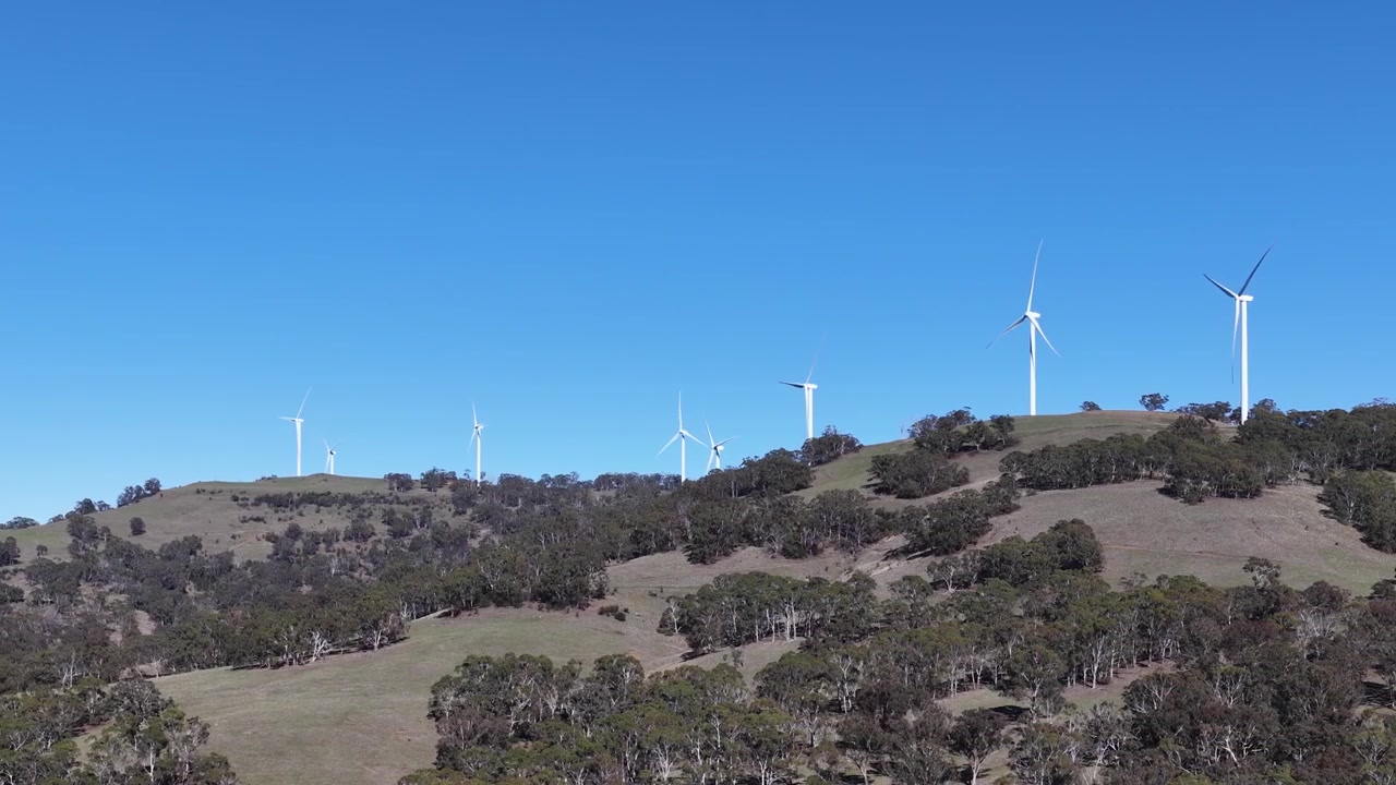 Turbine eoliche che ruotano sopra colline ondulate sotto un cielo luminoso e limpido nella campagna australiana