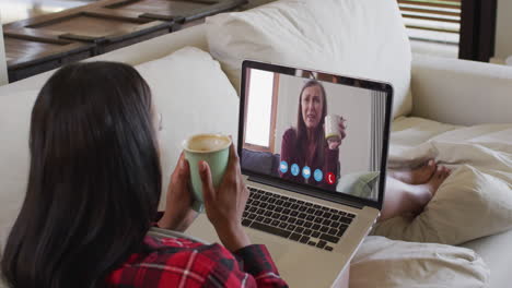 mujer biracial en chat de video portátil tomando café en casa