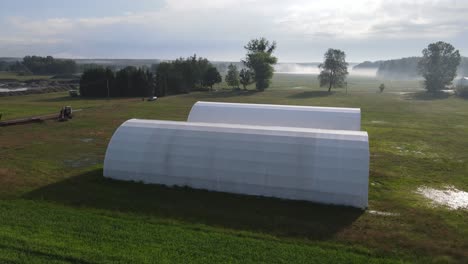 two white arched hall warehouse on farm aerial in sunny morning day