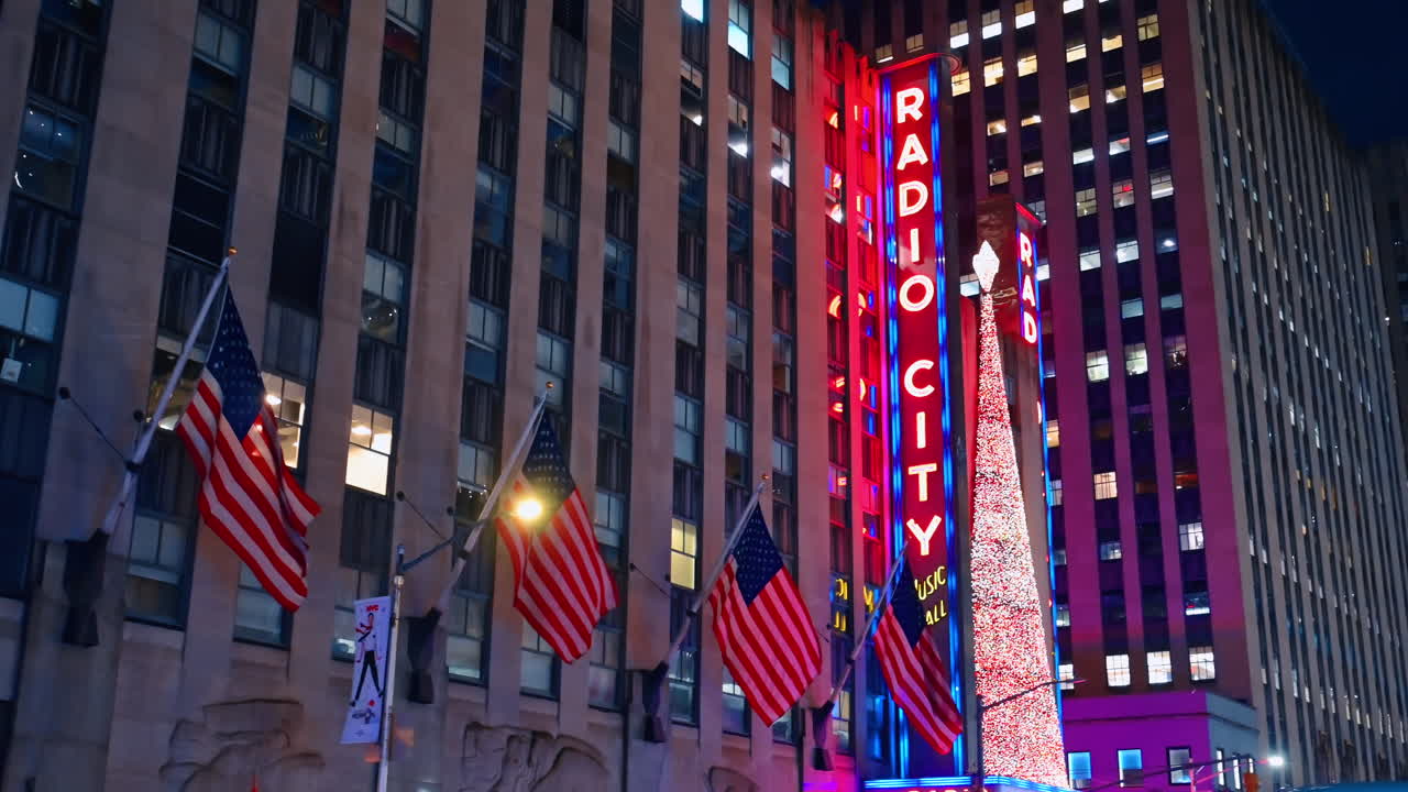 New York, ABD, 5 Aralık 2025: Amerikan Bayrakları ve Yılbaşı Ağacı ile Radio City Music Hall. Radio City Music Hall'un cephesi, Amerikan bayraklarını ve uzun, parıldayan Noel ağacı kurulumunu gece belirgin bir şekilde sergiliyor