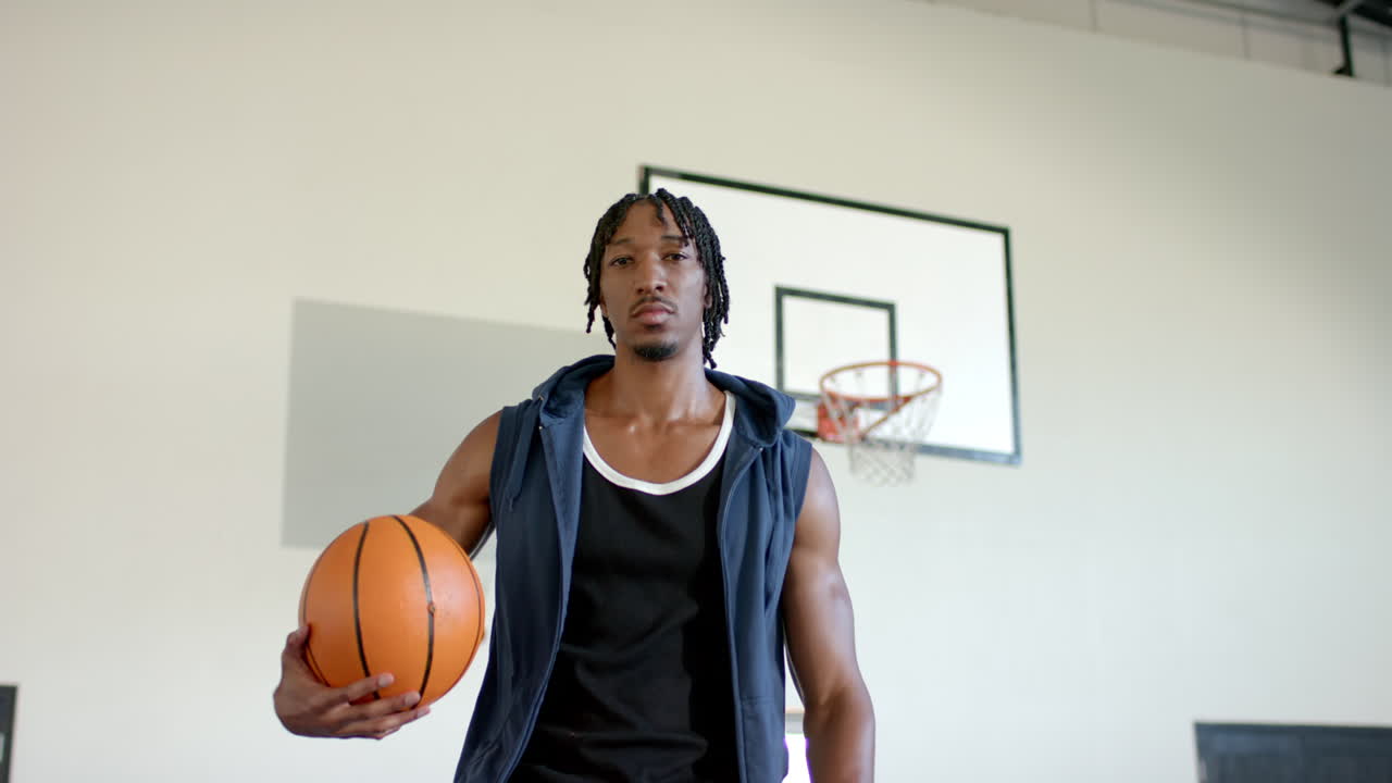 Holding basketball, man standing confidently in indoor school basketball court