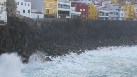 Grandes-Olas-Del-Océano-Atlántico-Se-Rompen-En-Una-Costa-Rocosa-En-Un-Día-Soleado-Durante-Una-Tormenta-En-Puerto-De-La-Cruz-En-Las-Canarias,-Casas-Distantes-Y-Coloridas,-Tiro-Ancho