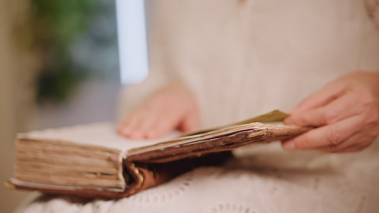 Anziana donna bianca che legge un libro antico, mani delicate sfogliano pagine ingiallite con un segnalibro a nastro d'oro, morbida e calda luce interna, si intravede un accogliente vestito di pizzo, primo piano intimo, ricordo di famiglia nostalgico, atmosfera lenta.