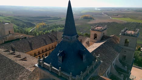 drone-flight-of-the-Ucles-monastery-seeing-as-the-central-image-the-black-roof-of-the-church-tower-located-on-one-side-with-a-beautiful-landscape-in-the-background-in-the-province-of-Cuenca