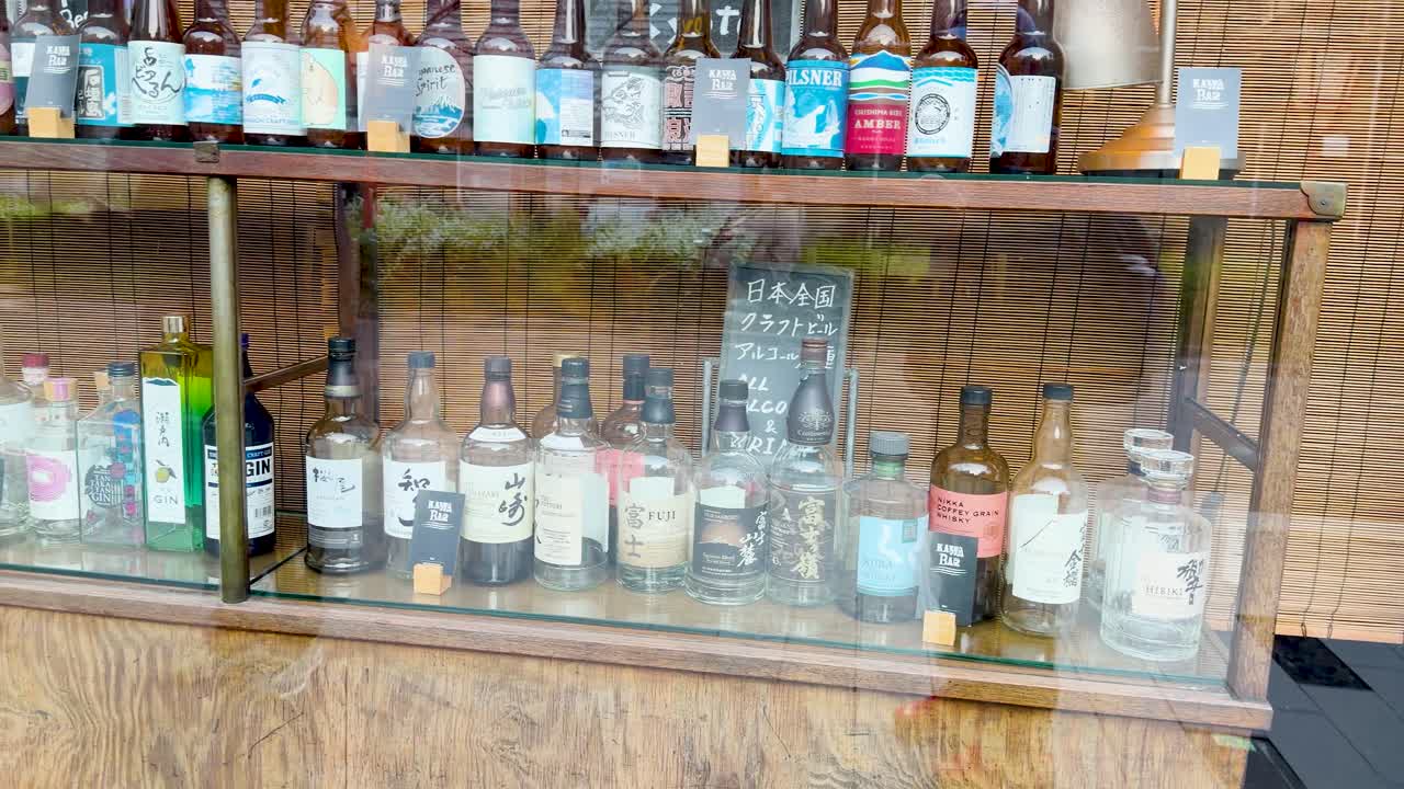 Una toma panorámica lenta a través de una vitrina de madera llena de botellas de licor japonés