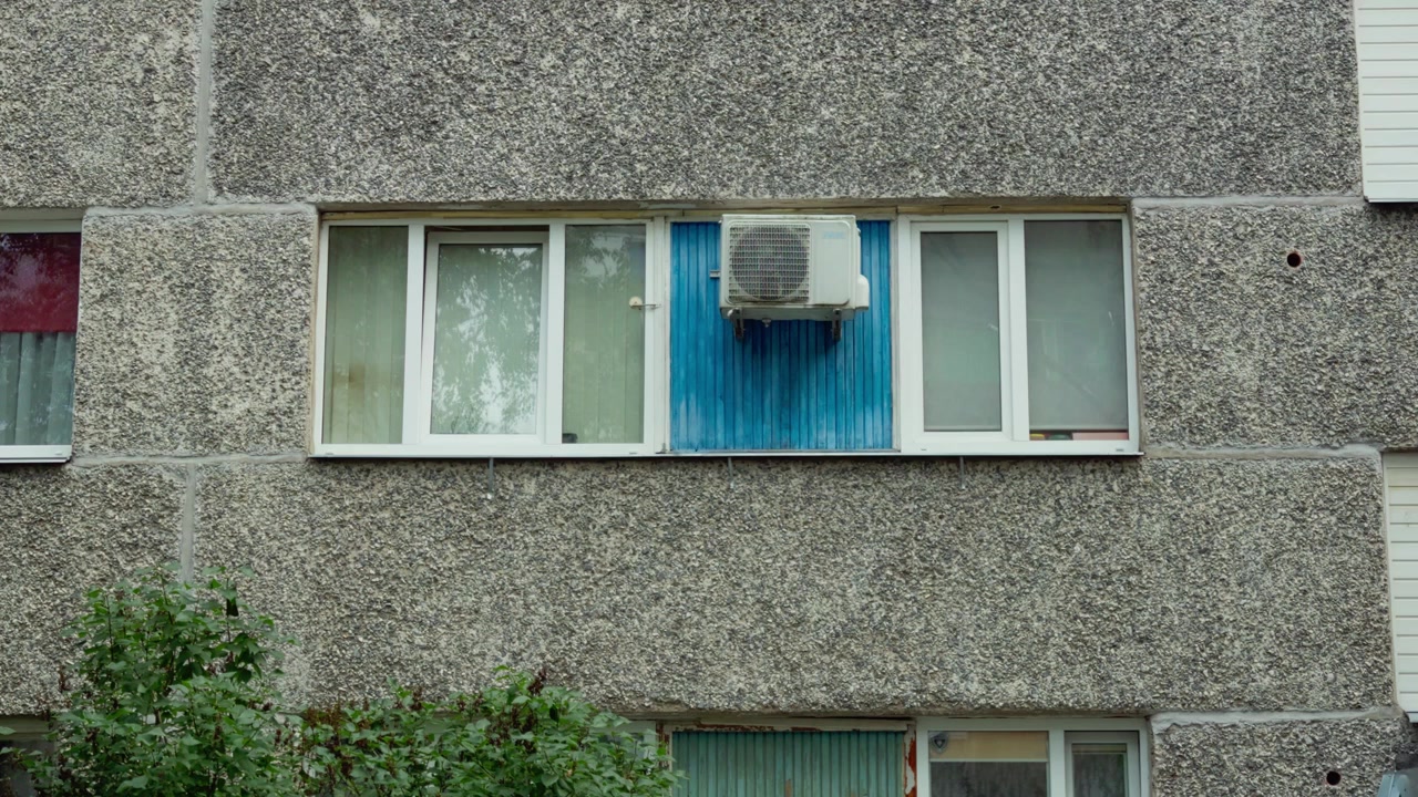 Primo piano statico di una moderna unità di condizionamento installata su un pannello blu brillante tra le finestre di un appartamento su una facciata in cemento testurizzato a Daugavpils, Lettonia