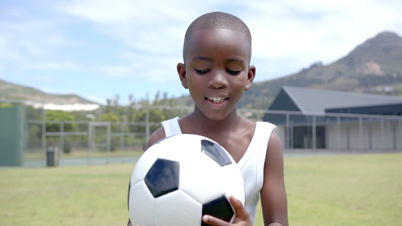 Na escola, criança segurando bola de futebol em campo, sorrindo e aproveitando esportes