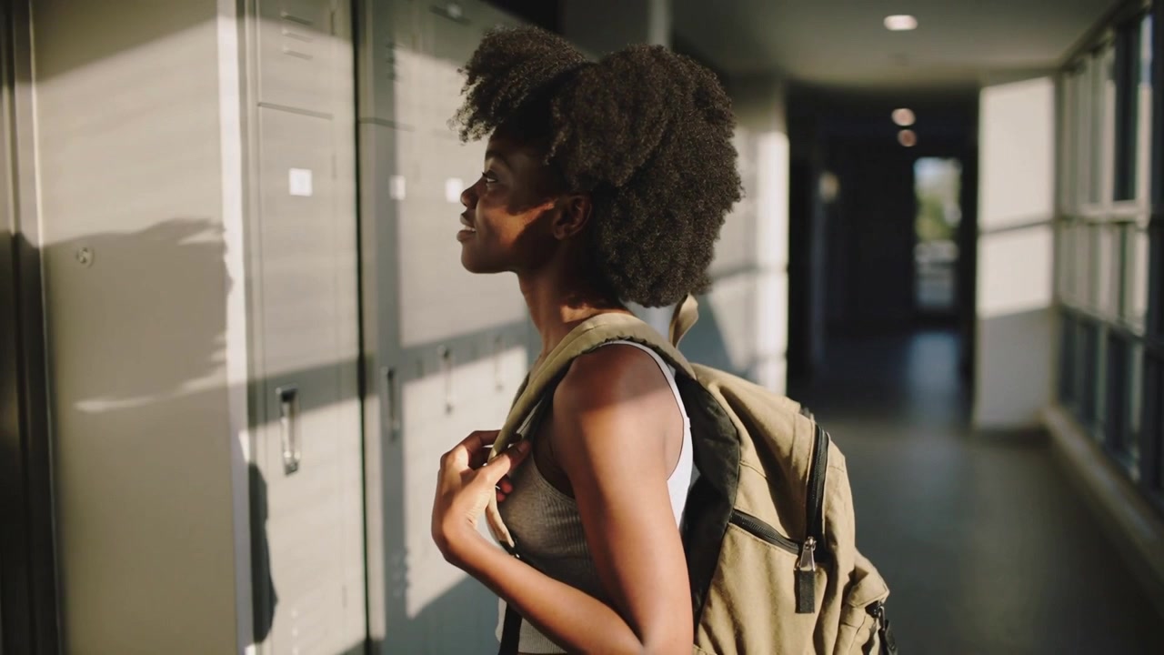 Spotting locker Black student in tank top holding backpack straps approaching school locker to open