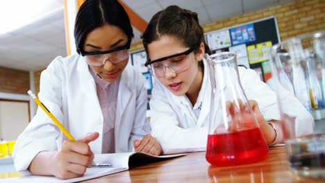 niñas escolares escribiendo en un libro de diario mientras experimentan en el laboratorio en la escuela