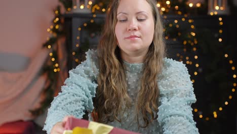 woman bows her head while handing over a gift box while smiling, static closeup