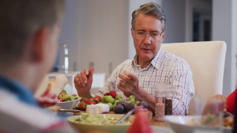 smiling caucasian grandfather talking to grandson at table during family meal